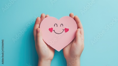 Hand Holding a Pink Paper Smile Symbolizing Emotional Mental Health and Love on a Blue Background, Top-down view, Heart-Shaped Smiley, Support Positivity, Wellness, and Happiness Concept