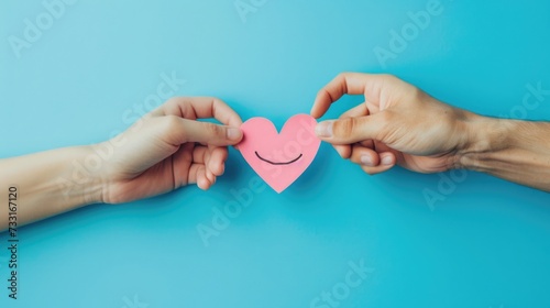 Hand Holding a Pink Paper Smile Symbolizing Emotional Mental Health and Love on a Blue Background, Top-down view, Heart-Shaped Smiley, Support Positivity, Wellness, and Happiness Concept