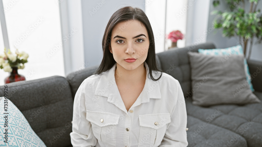 Portrait of a young hispanic woman sitting in a modern living room, looking confident and composed. Portrait of a young hispanic woman sitting in a modern living room, looking confident and composed.
