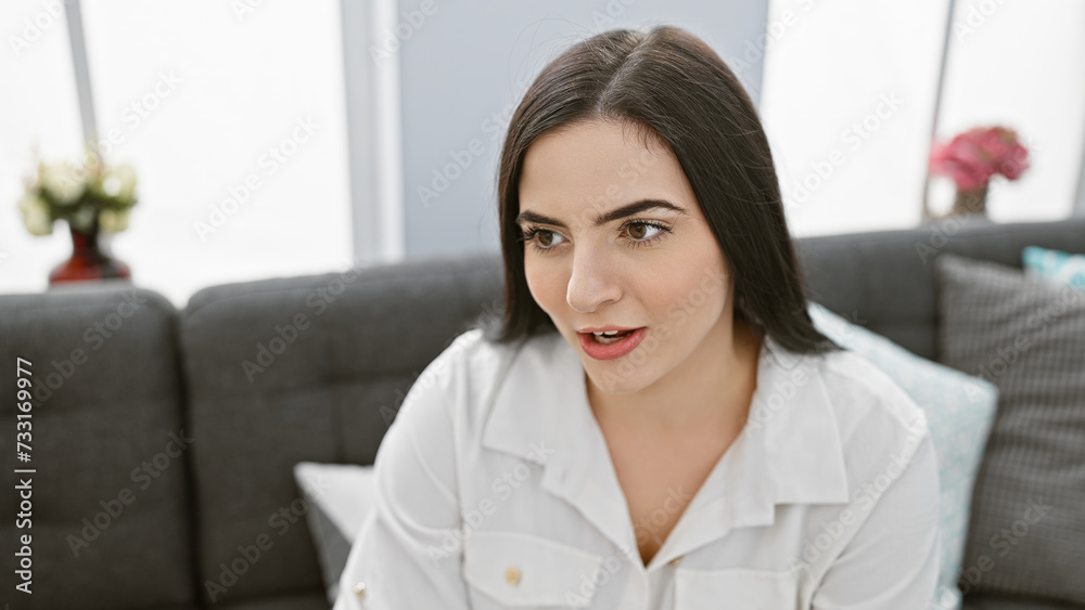 A young hispanic woman indoors looks away thoughtfully, embodying beauty and casual home living. A young hispanic woman indoors looks away thoughtfully, embodying beauty and casual home living.