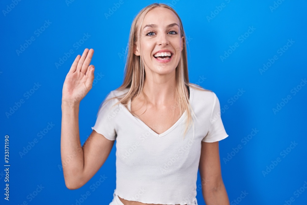 Fototapeta premium Young caucasian woman standing over blue background smiling positive doing ok sign with hand and fingers. successful expression.