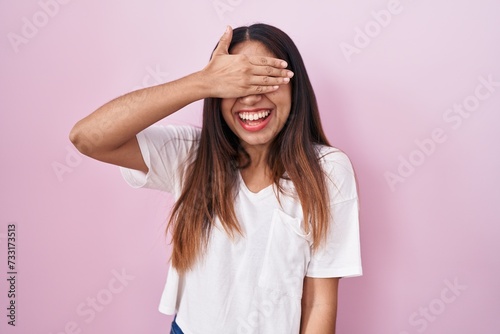 Young arab woman standing over pink background smiling and laughing with hand on face covering eyes for surprise. blind concept.