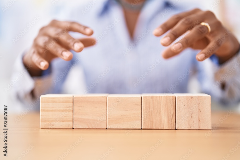 Middle age african american woman business worker sitting on table with wooden cubes at office Middle age african american woman business worker sitting on table with wooden cubes at office