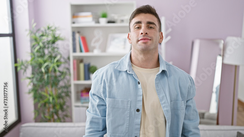 Young hispanic man standing with serious expression at home