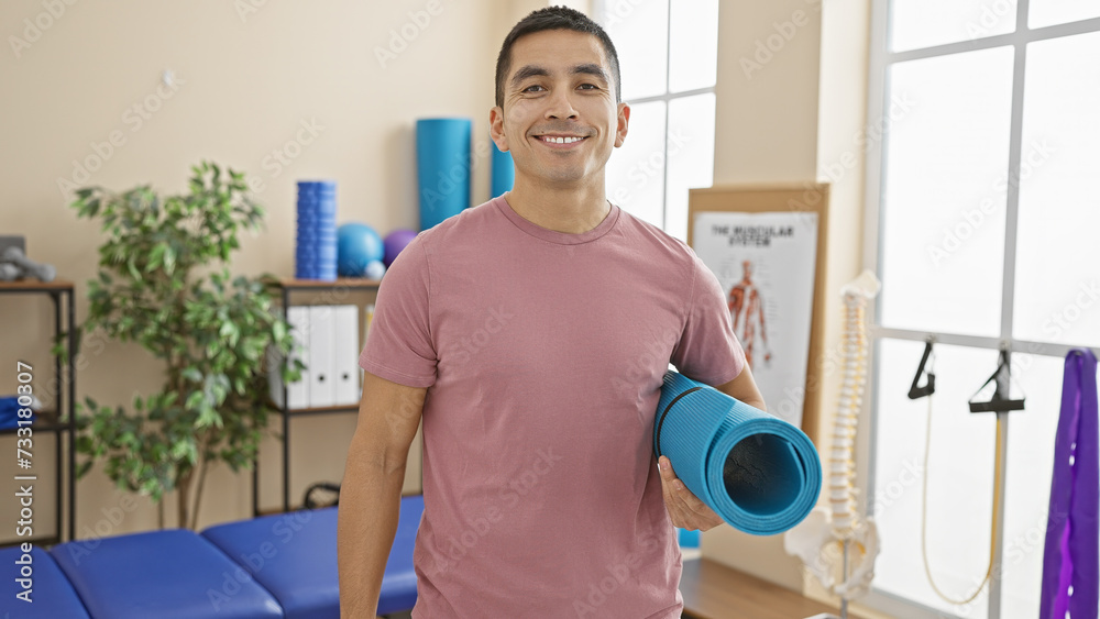 Handsome hispanic man holding yoga mat in a bright rehab clinic. Handsome hispanic man holding yoga mat in a bright rehab clinic.