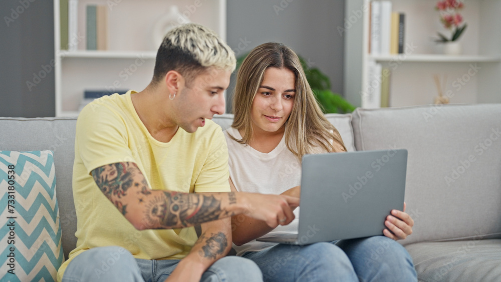 Beautiful couple using laptop sitting on sofa smiling at home