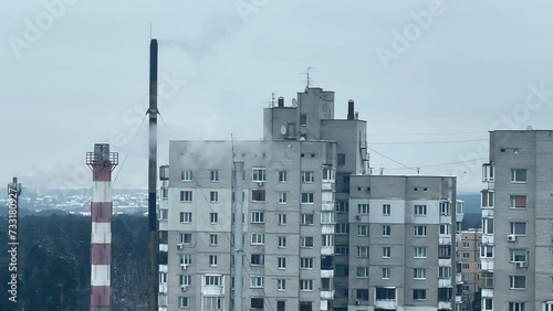 A toxic chimney of an enterprise against the background of the sky and the city releases smoke. The factory pollutes the environment. Industrial cityscape. Winter day. Poisoned air.