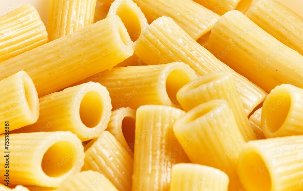 Close-up image of uncooked pasta rigatoni on a yellow background, capturing the texture and shape. Close-up image of uncooked pasta rigatoni on a yellow background, capturing the texture and shape.