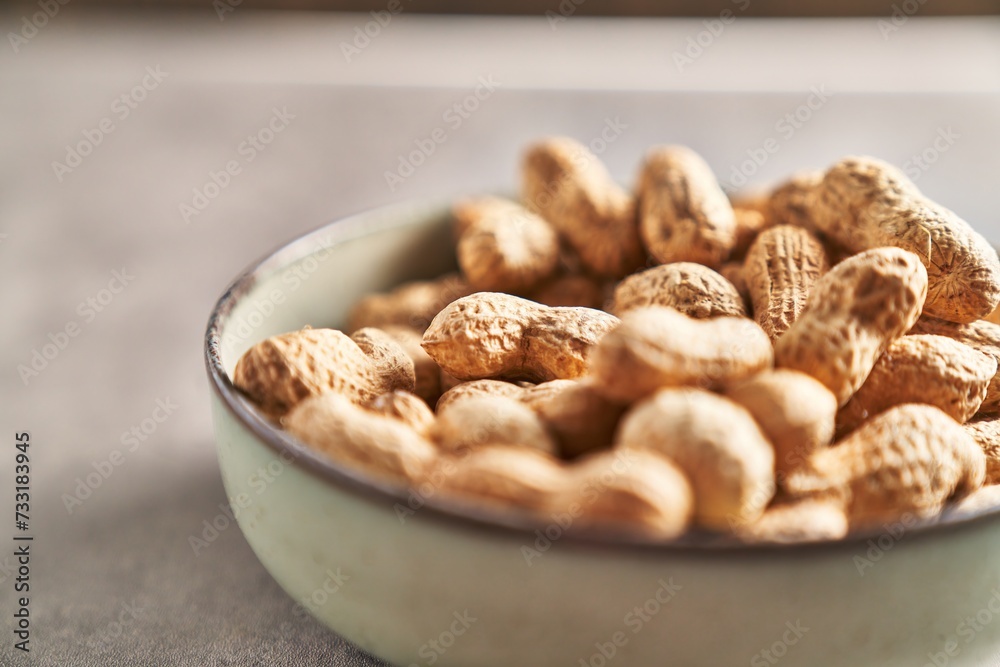 Close-up of unshelled peanuts in a bowl on a textured tabletop, hinting at healthy snacking.