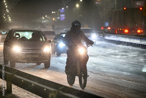 Zimą człowiek na motocyklu jedzie ślizgom drogą. 