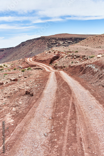 A winding dirt road snakes through a rugged desert landscape under a blue sky, conveying a sense of adventure and isolation.