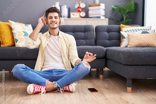 Young hispanic man doing yoga exercise sitting on floor at home