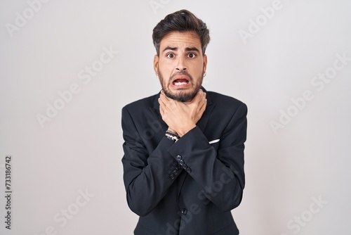 Young hispanic man with tattoos wearing business suit and tie shouting suffocate because painful strangle. health problem. asphyxiate and suicide concept.