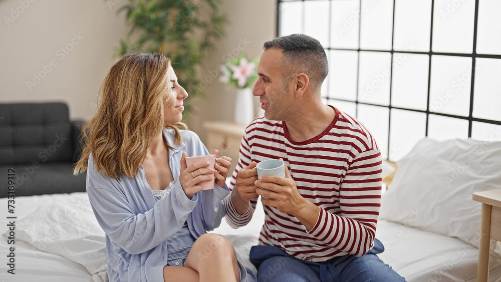 Man and woman couple sitting on bed drinking coffee at bedroom