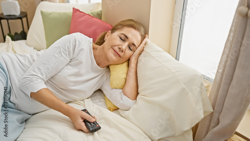 Mature caucasian woman relaxing in bedroom with remote