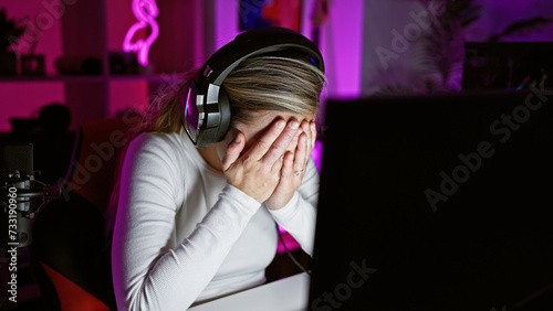 Принти на полотні Stressed woman in headphones faces gaming computer in a dark room with colorful neon light