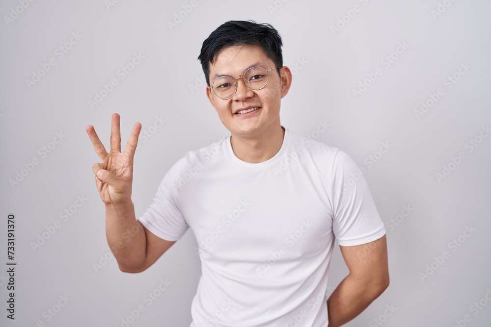 Young asian man standing over white background showing and pointing up with fingers number three while smiling confident and happy. Young asian man standing over white background showing and pointing up with fingers number three while smiling confident and happy.
