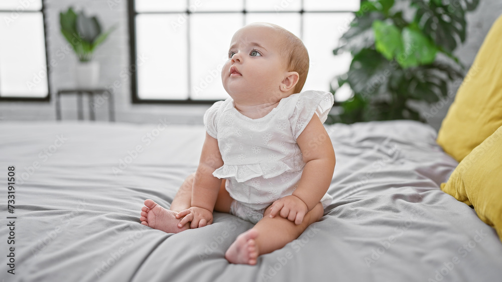 Adorable baby, a little toddler in comfy clothes, sitting relaxed on the bed sheet with a serious face in the morning! indoor lifestyle in the infant's room that exudes comfort and relaxation Adorable baby, a little toddler in comfy clothes, sitting relaxed on the bed sheet with a serious face in the morning! indoor lifestyle in the infant's room that exudes comfort and relaxation