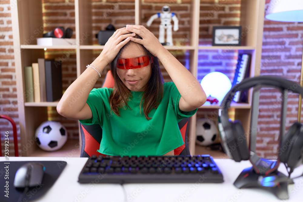 Middle age chinese woman wearing virtual reality glasses suffering from headache desperate and stressed because pain and migraine. hands on head.