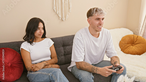 A man playing video games in a living room while a woman sits beside him  both young adults sharing a moment indoors.