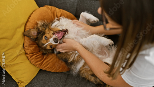 A young woman enjoys leisure time with her fluffy dog on a cozy couch inside a tastefully decorated house.