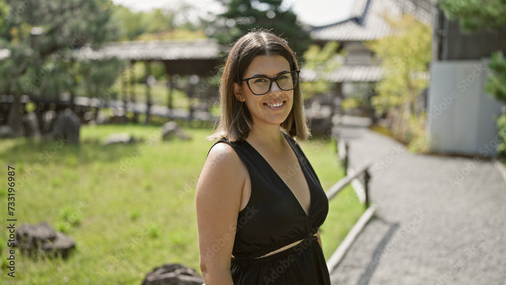 Cheerful beautiful hispanic woman, proudly posing with her glasses on, flashing a gorgeous smile at kyoto's serene kodaiji temple