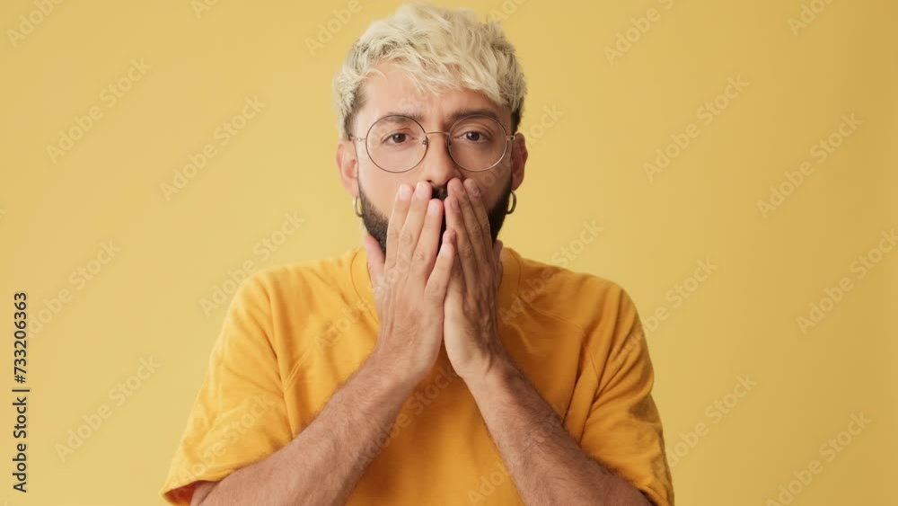Man looking at camera with big eyes, says wow, isolated on yellow background in studio