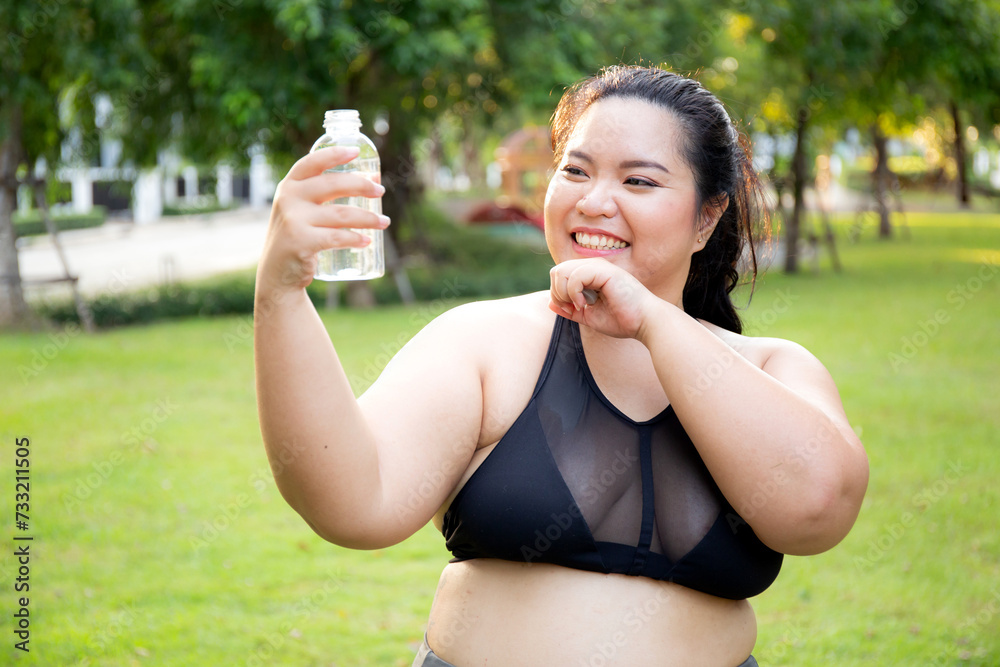Active plus size woman hydration drinking a water bottle outdoors, taking a break during a sunny day exercise routine, fat woman drinking water after workout in garden, activity for health.