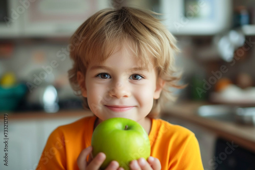 A smiling boy in an orange T-shirt holds a green apple in his hand