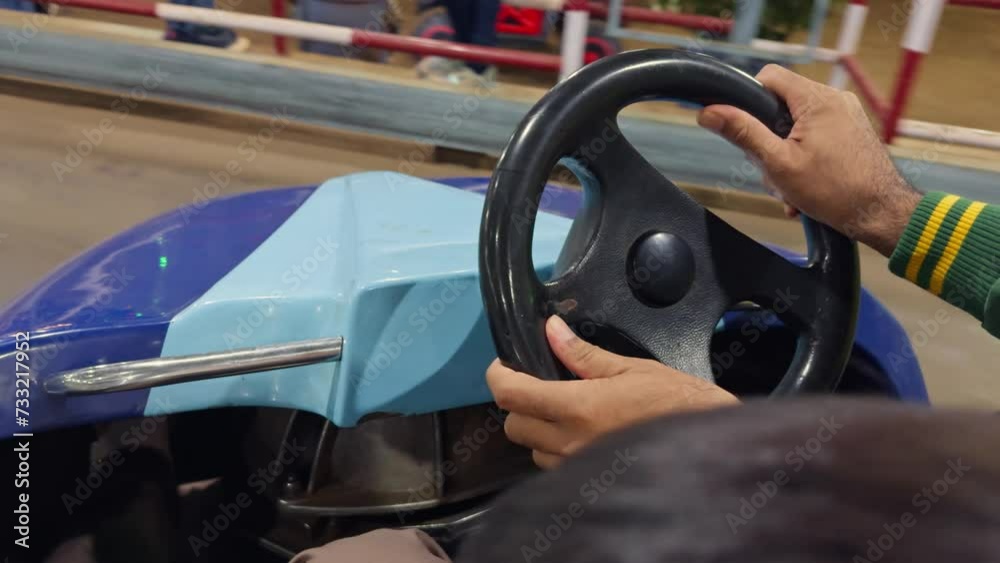 closeup man hand on a bumper car steering wheel with colorful cars in the background at an amusement park closeup man hand on a bumper car steering wheel with colorful cars in the background at an amusement park
