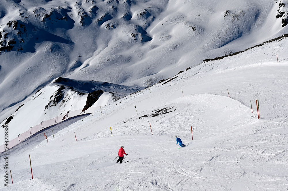 Two skiers on a steep slope with an impressive snowy mountain range in the background