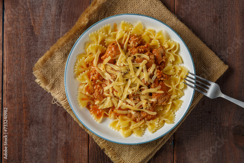Bolognese pasta in a plate on a linen napkin next to a fork on a wooden table