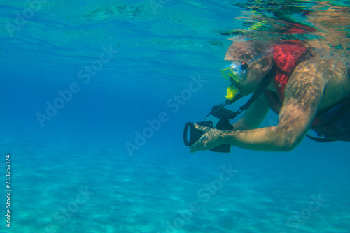 Man with photo camera taking photos and snorkeling underwater by coral reef in the Red sea, Egypt