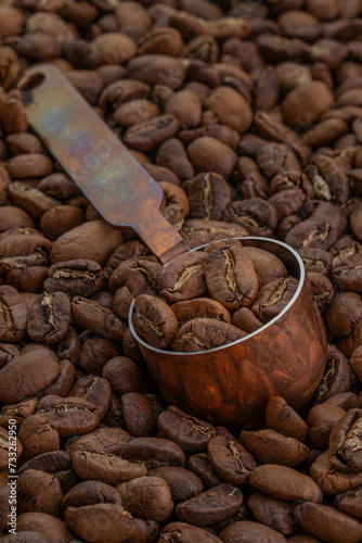 Hand-roasted Arabica Maragogipe coffee beans in a copper measuring spoon resting on top of the freshly roasted beans.