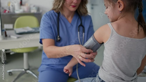 Doctor examining young girl, measuring blood pressure, using medical blood pressure monitor. Concept of preventive health care for children.