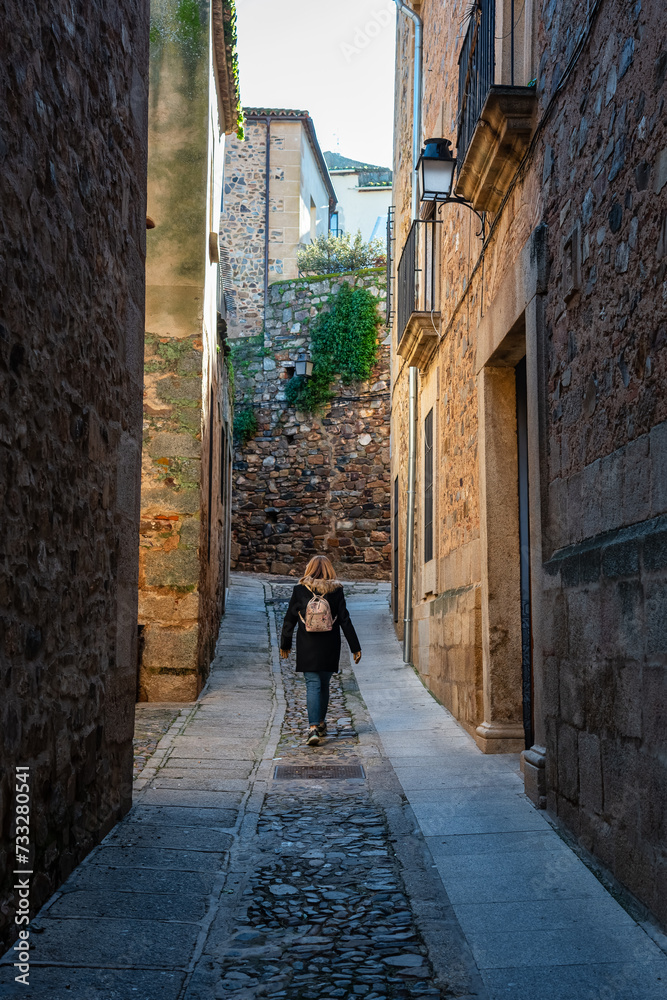 Female tourist strolling through the narrow streets of the medieval town of Caceres, Spain.