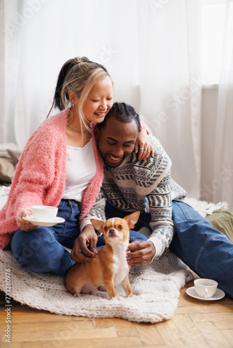 Positive asian woman with coffee hugging african american boyfriend near pet in bedroom © Dmytro Hai