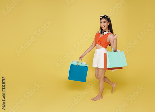 Portrait smiling attractive Asian woman in summer dress holding shopping bag summer sale isolated on yellow background.