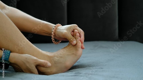 Foot pain, Asian woman sitting feeling foot pain at home, woman suffering from foot pain using hand massage to relax muscles from soles of feet photo