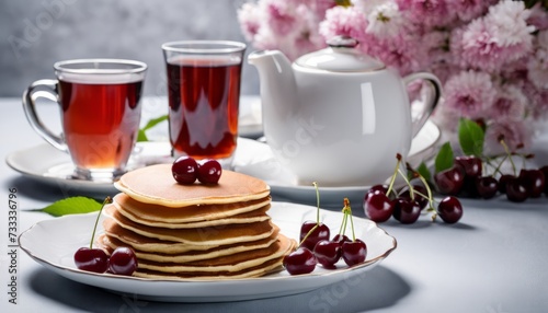 A stack of pancakes with cherries on top and two cups of tea
