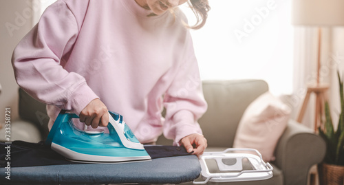 clothes, appliance, home, housework, iron, ironing, laundry, steam, clean, domestic. close-up young woman's hand using electric steam, water vapor from iron press pile shirt clothes on an ironing. photo
