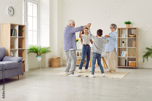 Family having fun at home. Joyful children and grandparents spend free time together. Cheerful, happy grandmother, grandfather and little kids dancing in a circle in a big, light, spacious living room © Studio Romantic