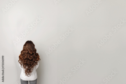 Femme de dos, avec des cheveux longs ondulés et portant un jean et un pull avec une emmanchure bateau. Espace négatif pour texte, copyspace  photo