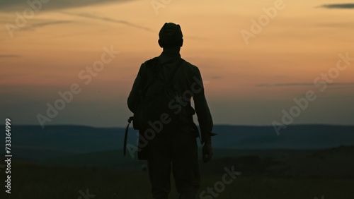 Silhouette of lonely soldier walking in field on red sunset background. A sad conceptual scene about the history of the soldiers of World War II and the Cold War. photo