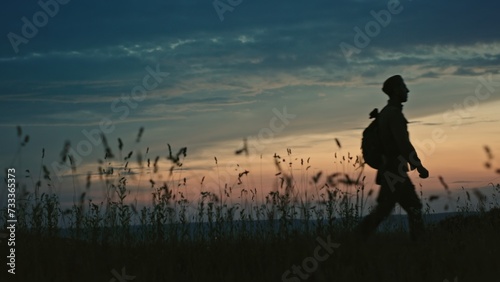 Soldier in uniform silhouetted against the sunset walking towards the camera across open countryside