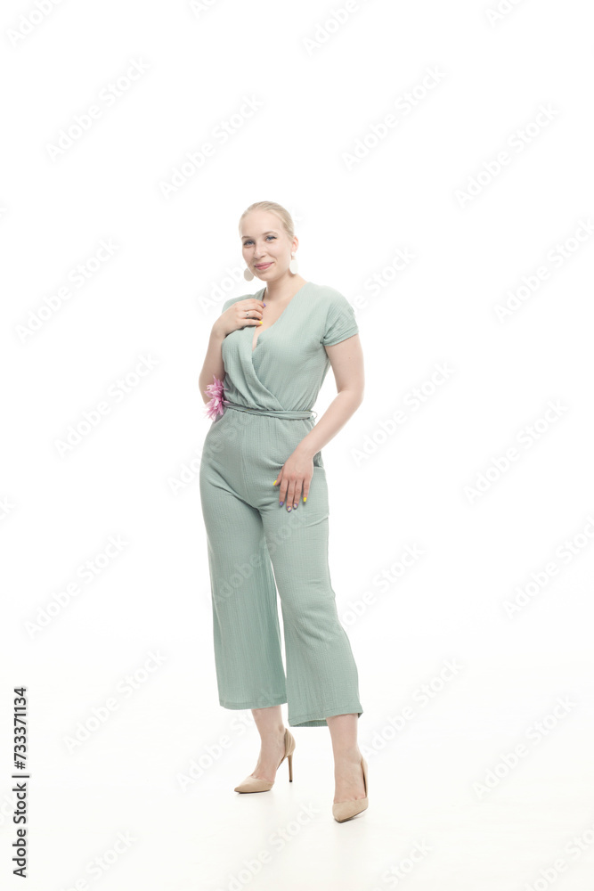 Fototapeta premium Young blonde woman in a mint knitted overalls on a white background.