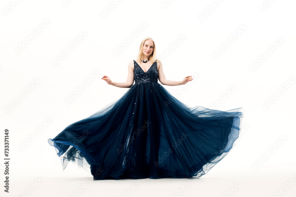 Young blonde woman in a dark blue ball gown with a fluffy skirt on a white background. Young blonde woman in a dark blue ball gown with a fluffy skirt on a white background.