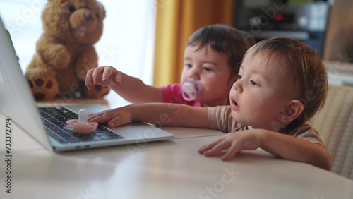 twin baby children a playing laptop watching video in the kitchen. happy family kid dream concept. baby twins playing video game lifestyle on laptop looking at screen in kitchen