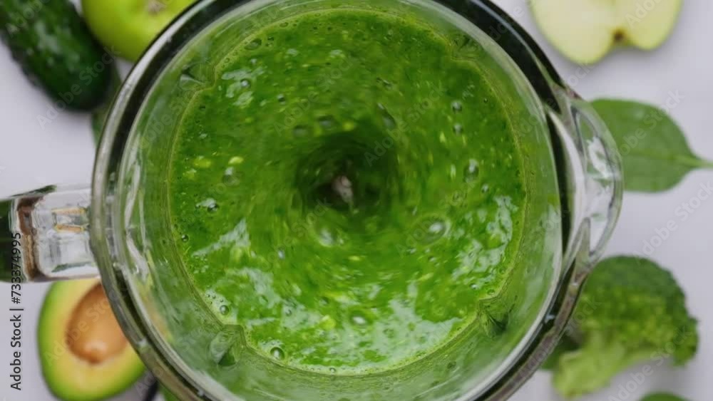 Green detox smoothie blended in blender. Cooking healthy drink from green vegetables, fruits and leaves blended in blender. Slow motion. Healthy detox drink concept. Top view Green detox smoothie blended in blender. Cooking healthy drink from green vegetables, fruits and leaves blended in blender. Slow motion. Healthy detox drink concept. Top view