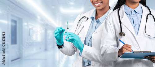 Fototapeta Naklejka Na Ścianę i Meble -  A female doctor in a white coat preparing a vaccine with a syringe is accompanied